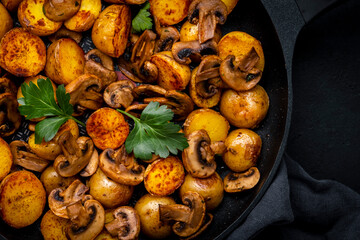 Baked golden potatoes with mushrooms in frying pan. Black background, top view