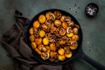 Baked golden potatoes with mushrooms in frying pan. Black background, top view