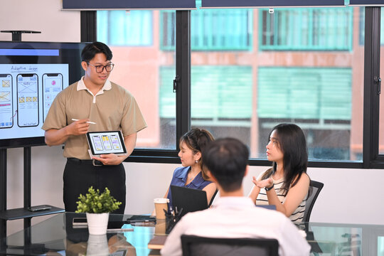 Man showcasing mobile app interface designs on digital tablet during team meeting in a modern office