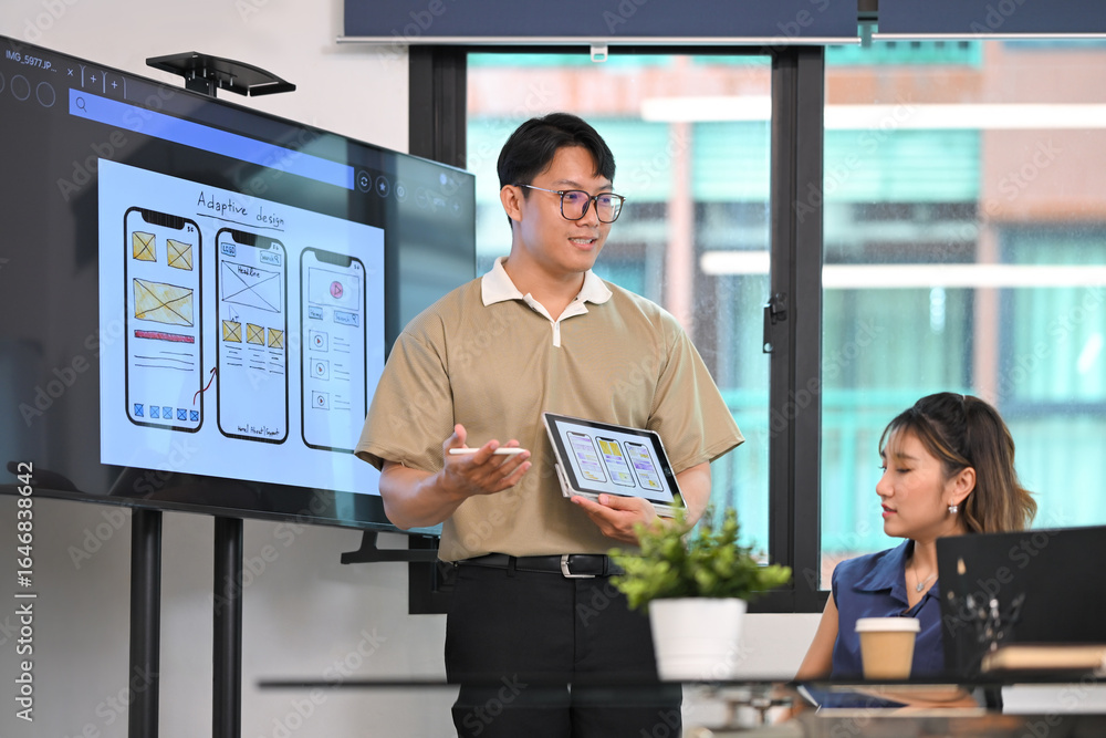 Poster man presenting mobile app interface wireframes on digital tablet during a team brainstorming