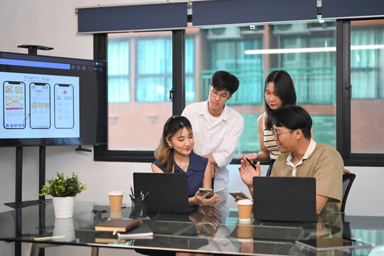 Young creative professionals discussing mobile app UI design during a team meeting - Powered by Adobe