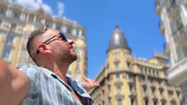 POV Point of view of male latin cheerful traveler tourist spreading arms wide, basking in summer sunlight near Callao Square, embodying pure joy and freedom of Madrid adventure.