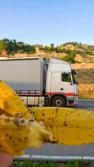 Close-up of soiled yellow gloves holding debris, blurred truck and landscape in background
