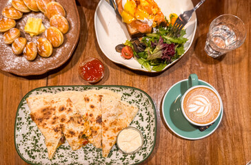 Flat lay of a cafe meal featuring Dutch poffertjes with butter, cheesy quesadillas, toast with...