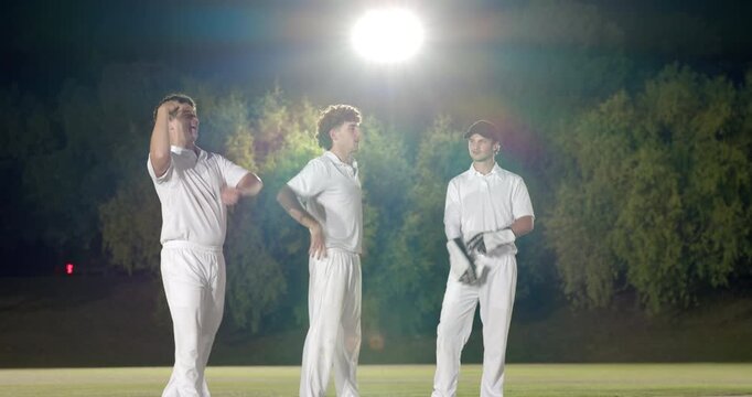 Diverse cricket teammates appealing on floodlit pitch, removing gloves and batsman entering crease - Powered by Adobe