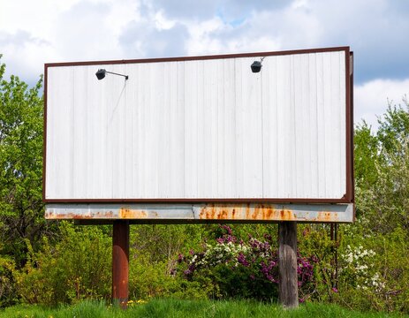 Large blank weathered billboard with a rusty metal frame, ready for advertising mockups in an outdoor nature setting.