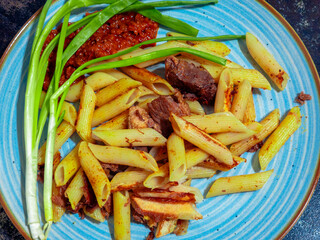 Penne pasta with meat, green onions and adjika on a blue plate