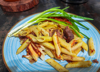 Penne pasta with meat and green onions seasoned with spices on blue plate