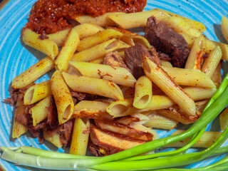 Penne pasta with meat, tomato sauce and spring onions served on blue plate