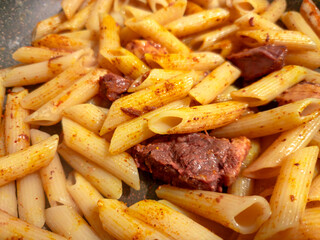 Penne rigate pasta with meat and spices cooking in a pan