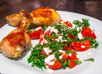 Roasted chicken legs and fresh salad with tomatoes and arugula lying on a plate