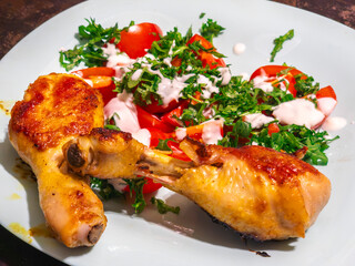 Two roasted chicken drumsticks served with fresh tomato and arugula salad dressed with yogurt sauce