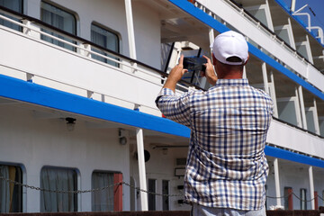 Tourist taking pictures of cruise ship with smartphone on sunny day