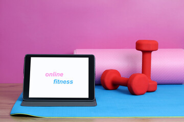 Online fitness class equipment displayed on yoga mat with tablet showing workout app
