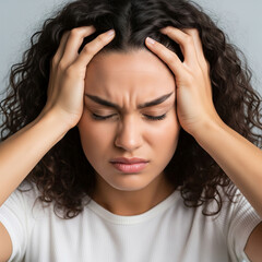 Fototapeta premium Stressed young woman with her eyes closed and hands gripping her head, expressing intense pain, anxiety, or frustration. Portrait conveys emotional distress, headache, and mental exhaustion.