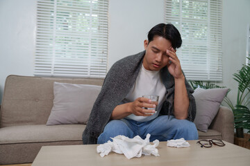Sick young man suffering from headache holding glass of water at home