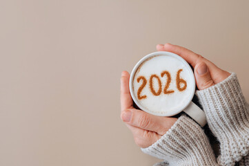 Woman in cozy sweater holding hot coffee with 2026 on milk foam, festive New Year concept