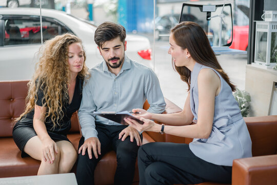 Young couple discussing car purchase with female sales agent in showroom, representing consultation, service quality, and satisfaction in automotive sales process.