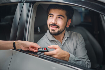 Smiling male customer sitting in new car receiving keys from dealer, symbolizing joy, satisfaction, and pride in automotive, insurance, and finance industry sales.