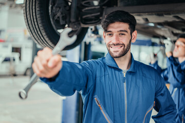 Male mechanic in blue uniform extending wrench toward viewer, showing trustworthiness, professional service, and quality repair in automotive maintenance industry.