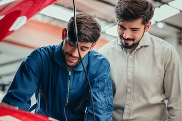 Mechanic and customer smiling while checking engine together, showing transparency, professional service, and positive customer experience in automotive repair workshop.