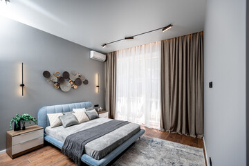 A bedroom with a blue bed, white pillows, and a gray blanket. The room has a modern design with a...