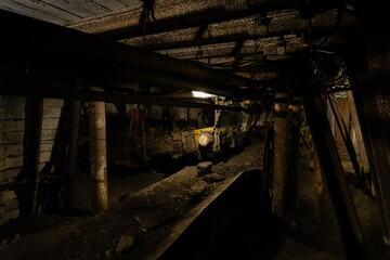 Dimly lit mining tunnel with ventilation pipes, cables and belt conveyor in an abandoned coal mine,...