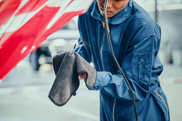 Mechanic in blue uniform cleaning dipstick with microfiber cloth, symbolizing quality check, professional service, and attention to detail in automotive maintenance.