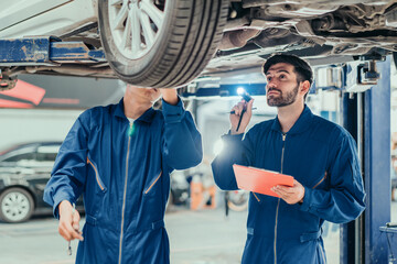 Mechanics in blue uniforms inspecting underside of car with flashlight and clipboard, symbolizing teamwork, professional service, and quality automotive repair.