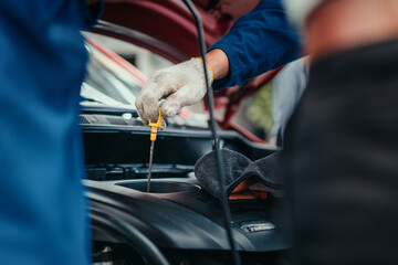 Mechanic checking engine oil with dipstick in workshop, representing detailed maintenance, professional service, and reliability in automotive repair.