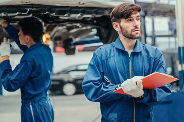 Mechanic reviewing service checklist on clipboard with colleague working in background, symbolizing quality inspection, professionalism, and trust in automotive repair.