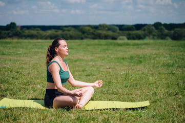 Calm young woman meditating outdoors in lotus position, practicing yoga and mindfulness for mental...