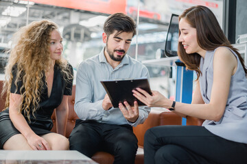 Young couple reviewing car purchase on tablet with female sales agent, symbolizing modern transaction, consultation, and customer satisfaction in automotive sales.