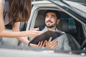 Smiling customer in new car looking at sales agent while reviewing agreement, symbolizing trust, satisfaction, and success in automotive sales.