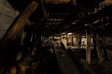 Dimly lit mining tunnel with ventilation pipes, cables and belt conveyor in an abandoned coal mine,...