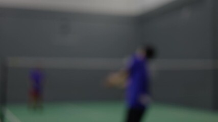 Blurry action shot of players training in an indoor badminton court, capturing speed and dynamic movement.
