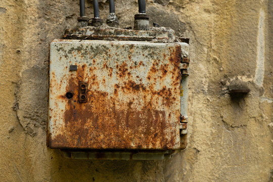 Rusted metal electrical enclosure on an exterior wall with conduits, showing heavy corrosion and weathered patina, urban industrial setting