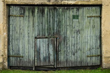 Old weathered wooden barn doors with peeling green paint and padlock on a rural outbuilding exterior