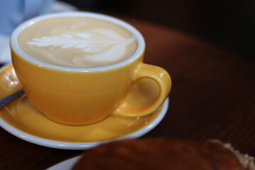 Delicious latte art on creamy coffee served in a vibrant yellow cup on a wooden table