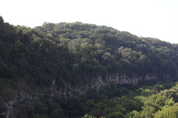 Lush green hillside with rugged cliff along the tranquil river valley in early morning light