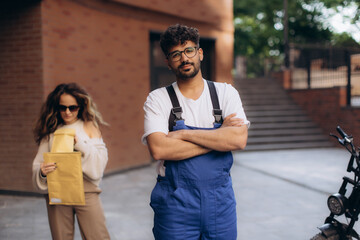 Delivery man waiting with crossed arms and electric scooter, woman holding package