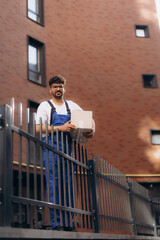 Delivery man holding package behind metal fence in residential area