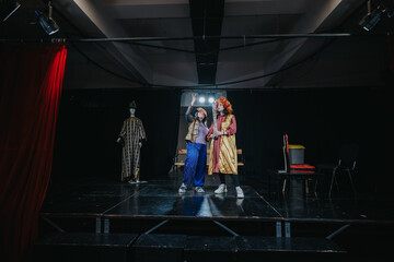 Actors dressed in colorful costumes are performing on a stage with theatrical lighting, showcasing...