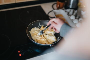 Close-up of a person stirring scrambled eggs in a pan while cooking on a modern electric stove.