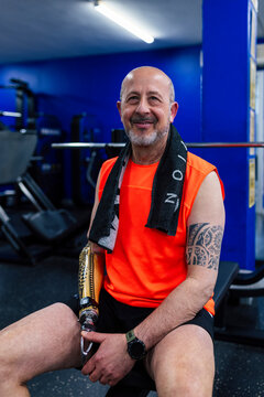 Man with prosthetic arm resting on bench in modern gym smiling
