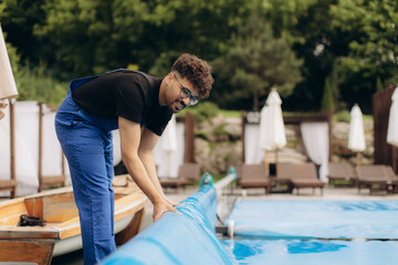 Pool maintenance worker rolling up cover at resort