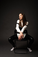 girl in leather pants in studio on black background, she sits on chair