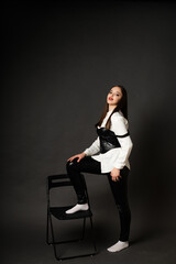girl in leather pants in studio on black background, she sits on chair