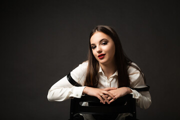 girl in leather pants in studio on black background, she sits on chair