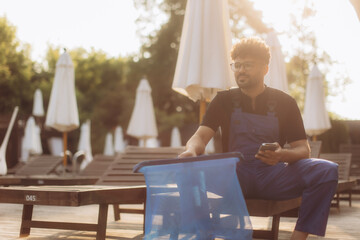 Pool cleaner relaxing on sunbed and browsing smartphone at sunset
